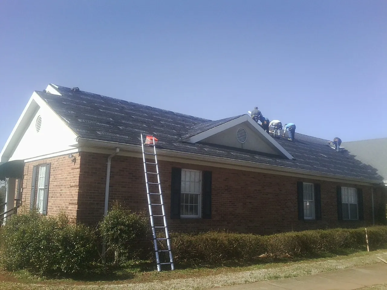 Crew tearing shingles off a brick ranch roof with a ladder set — Emergency Roof Repair work by our crew in Solon