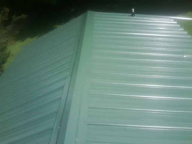New green metal panels meeting at the ridge of a roof — Flat Roof Repair work by our crew in Solon